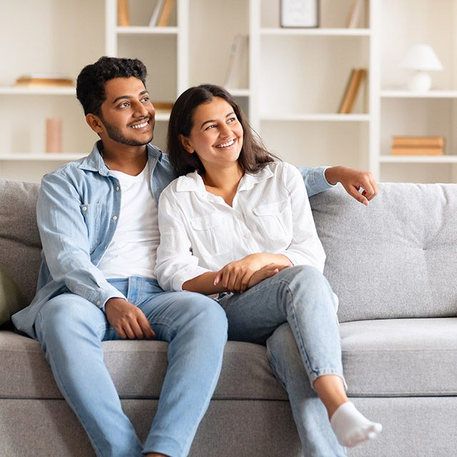 Happy couple, comfortably sitting on a sofa in their homey space
